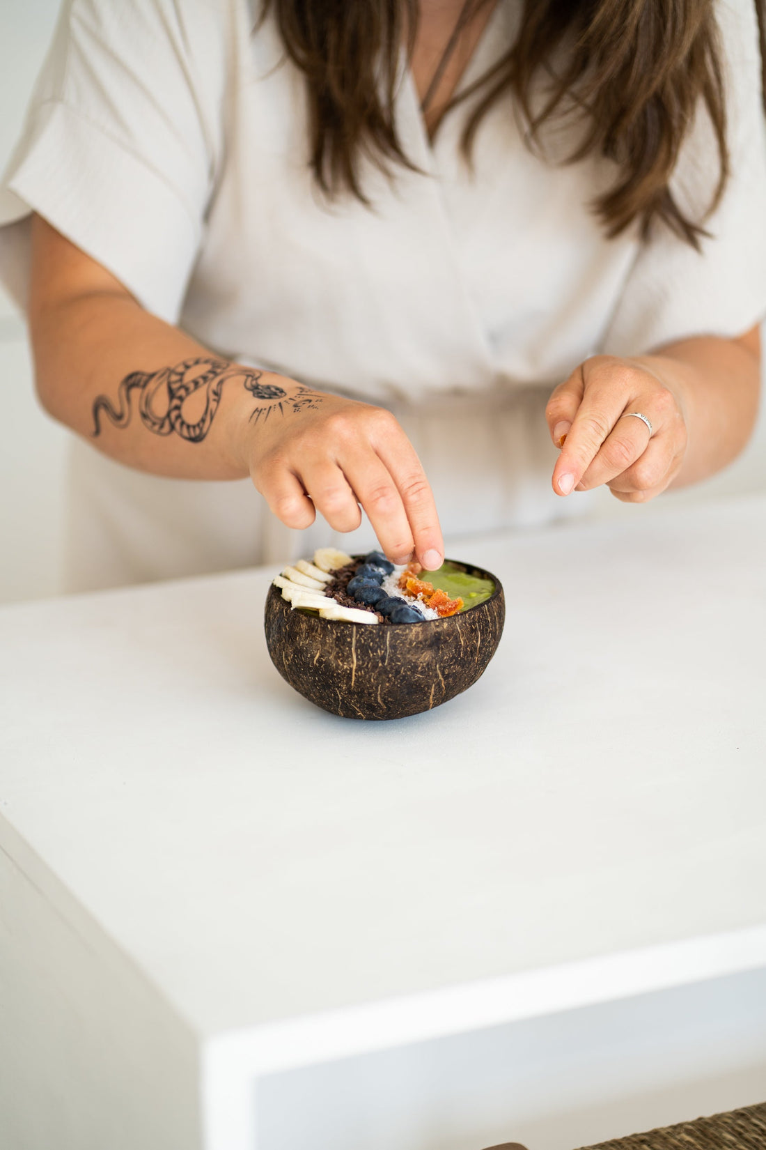 vrouw met arm tattoo vult een matcha bowl met fruit