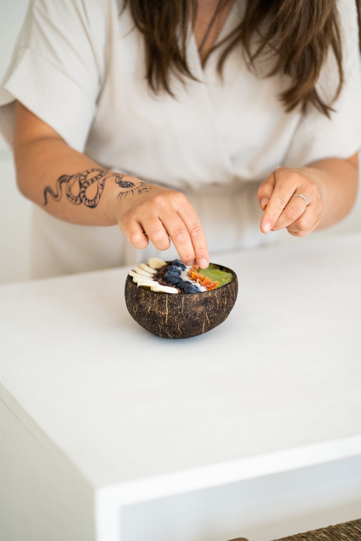 vrouw met arm tattoo vult een matcha bowl met fruit