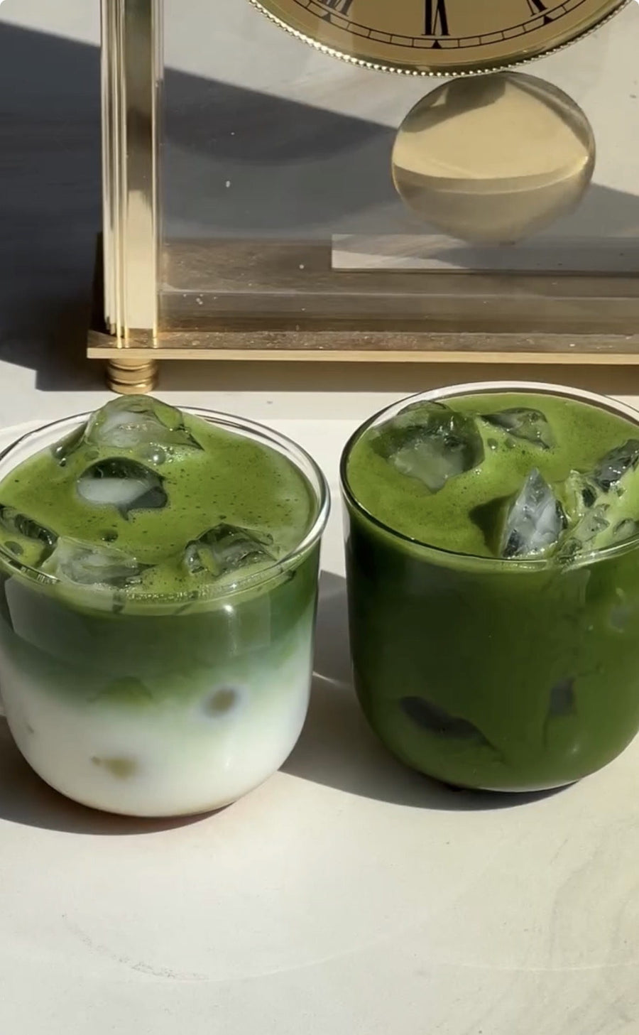 Zwei Gläser Iced Matcha in der Sonne, links mit Milch in getrennten Schichten und rechts ohne Milch