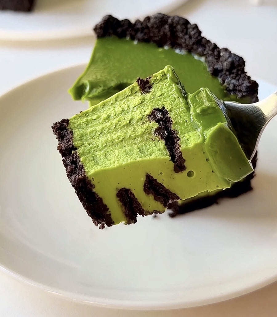 Bissen Matcha Cheesecake auf einer Gabel, mit durchgehend grüner Füllung auf einem dunklen Keksboden